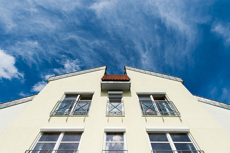 Blick von unten auf die helle Fassade eines Seniorenheims, vor blauem Himmel.